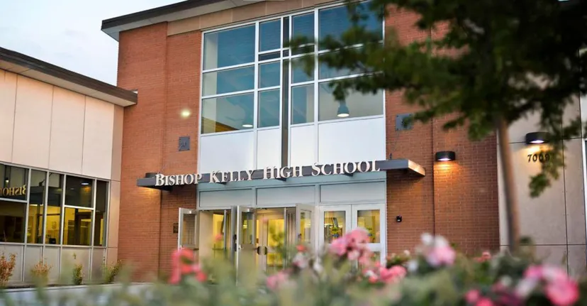 La vista esterna dell'edificio scolastico della Bishop Kelly High School con fiori rosa in fiore in primo piano.