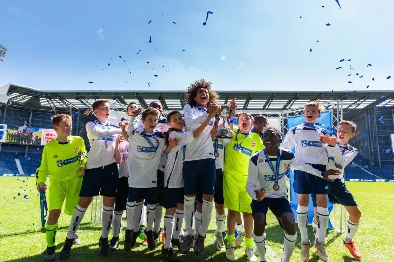 Alumnos de Whitgift School celebran juntos en el campo de fútbol con un estadio al fondo.