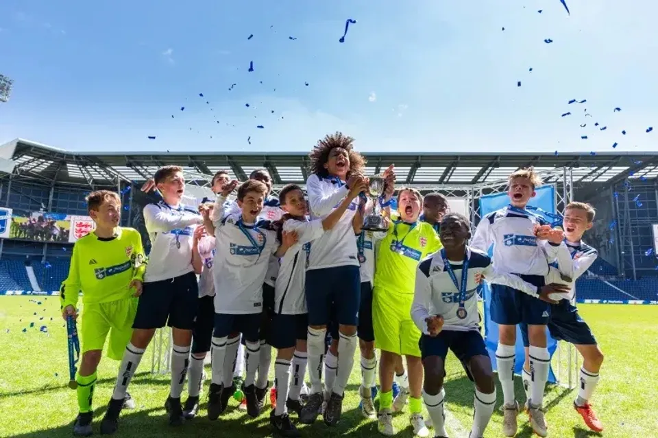 Studenti della Whitgift School festeggiano insieme sul campo da calcio con lo stadio sullo sfondo.