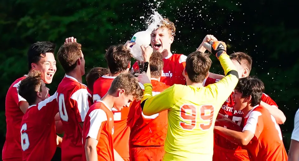 Studenti della Saint John‘s Prep festeggiano insieme durante un evento sportivo all'aperto con specchi d'acqua e immersi nel verde.