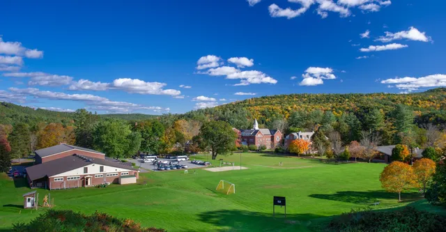Un campo da golf verde con foglie autunnali colorate e un villaggio con un campanile sullo sfondo, nel campus della Vermont Academy.