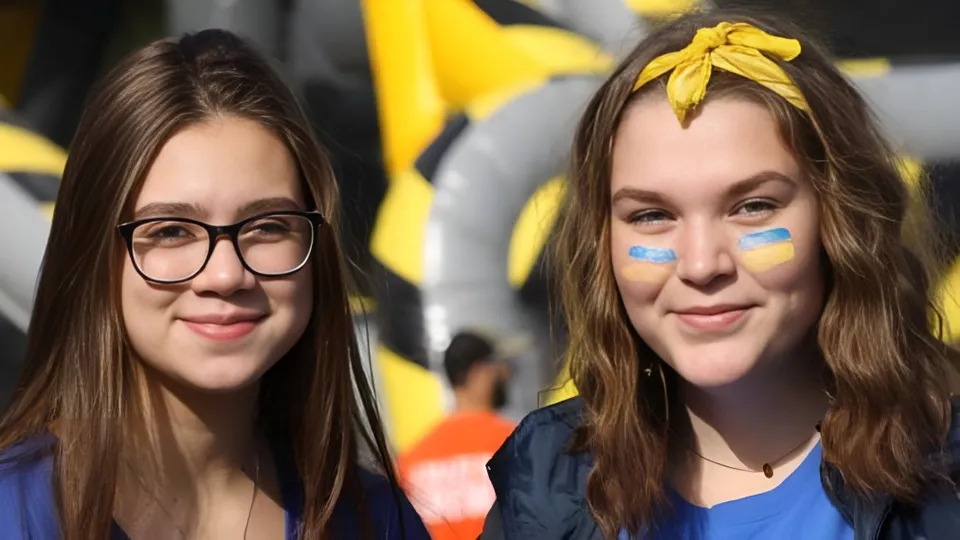 Due studentesse del Collège Notre-Dame con i capelli castani e il viso dipinto posano davanti a uno sfondo colorato.