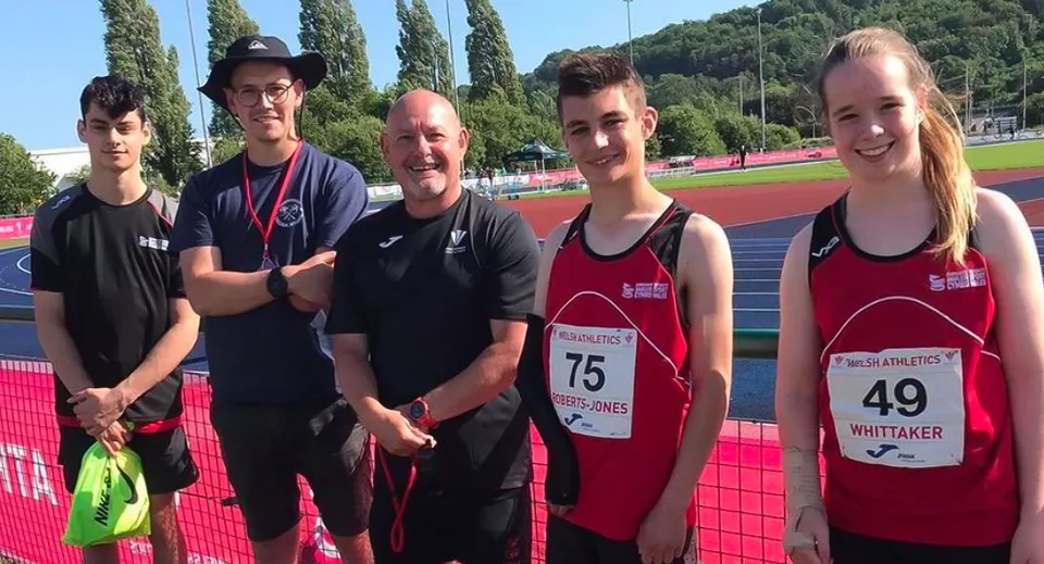 Un gruppo di atleti sta sulla pista da corsa del Myddelton College davanti ad alberi ed edifici.