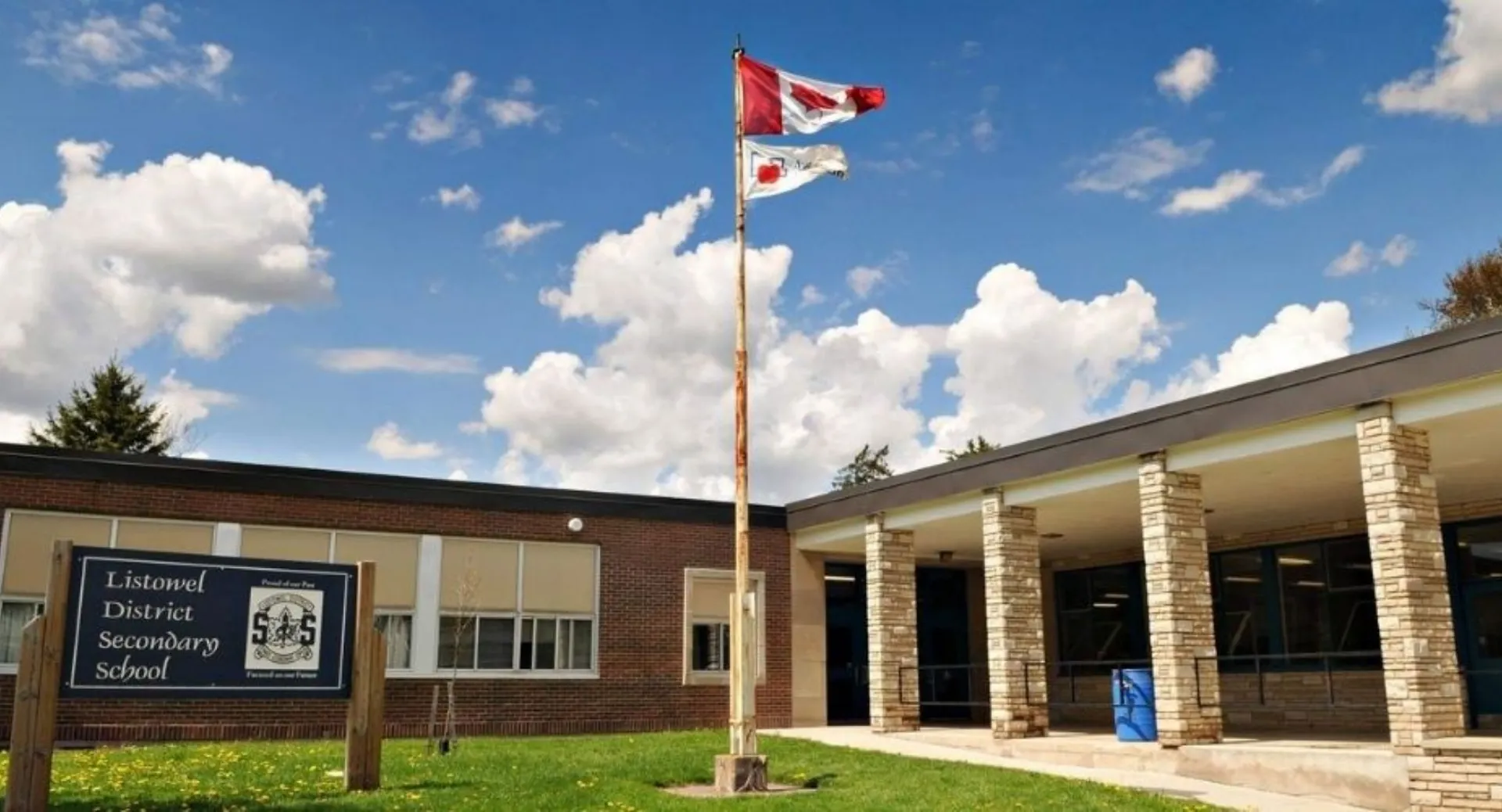 La bandiera canadese sventola sul tetto dell'edificio in mattoni della Listowel District Secondary School sotto un cielo nuvoloso.