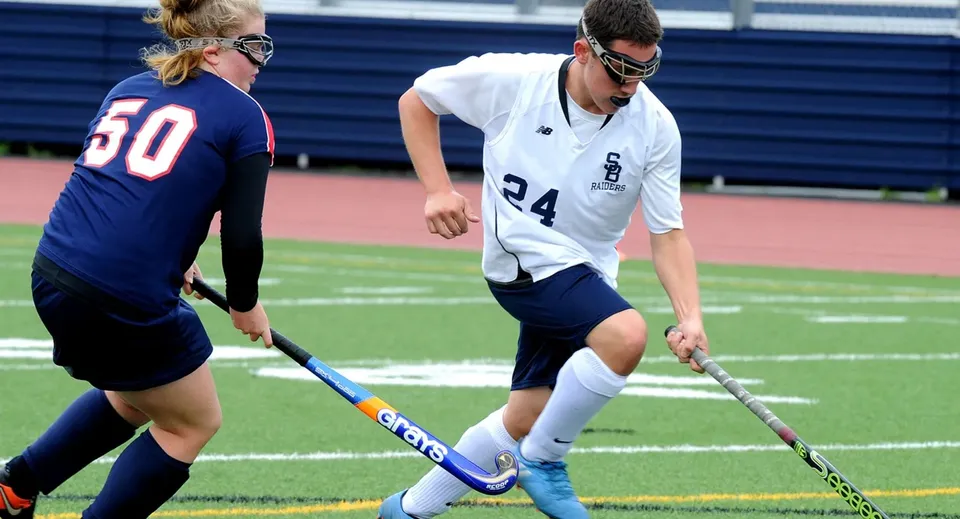 Due studenti della Ballinteer Community School giocano una partita di hockey su prato sul campo sportivo blu.