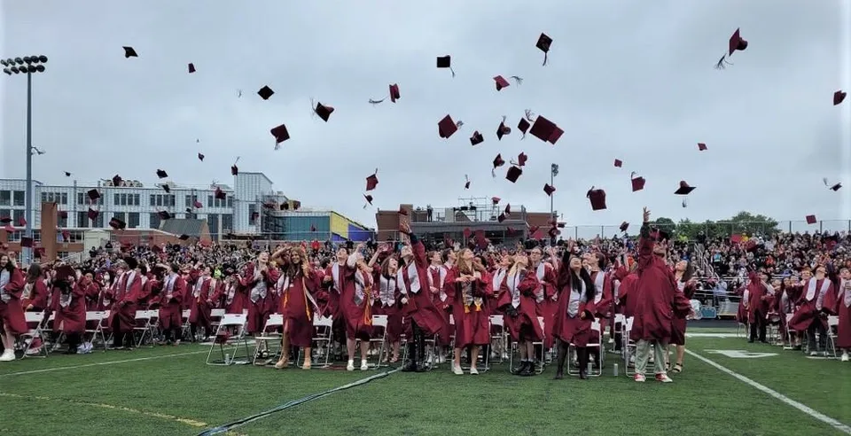 Un grande gruppo di diplomati della Arlington High School lancia in aria i propri tocchi durante la cerimonia di diploma su un campo.