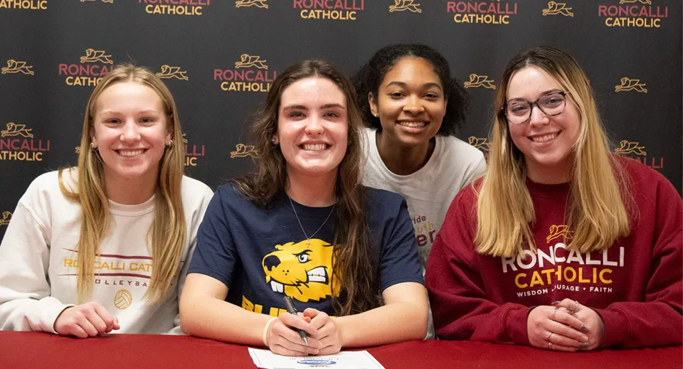 Quattro studentesse posano insieme davanti al logo della Roncalli Catholic High School.