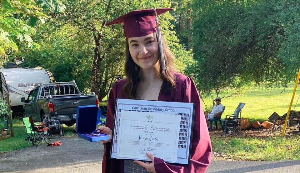 Una diplomata della Cowichan Secondary School si trova all'aperto con il suo diploma in mano.