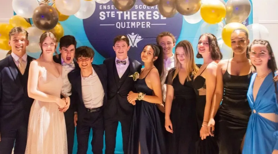 Un gruppo di studenti e studentesse in abito formale posa davanti a uno sfondo con la scritta Lycée Sainte Thérèse Quimper.