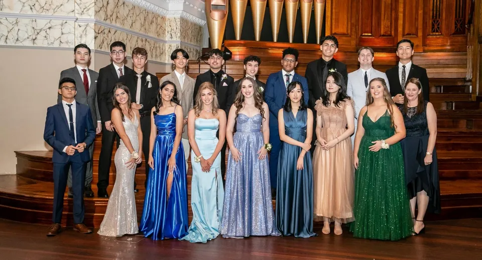 Un gruppo di persone vestite in modo formale è in piedi davanti a un grande organo negli sfarzosi interni del James Hargest College.