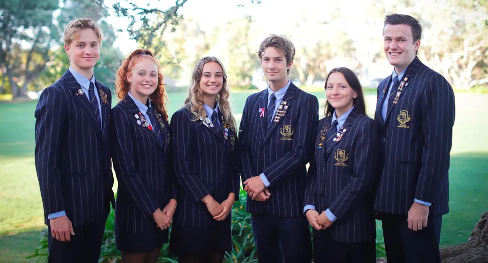 Un gruppo di studenti della Takapuna Grammar School si trova insieme in un'area simile a un parco con alberi e spazi verdi.