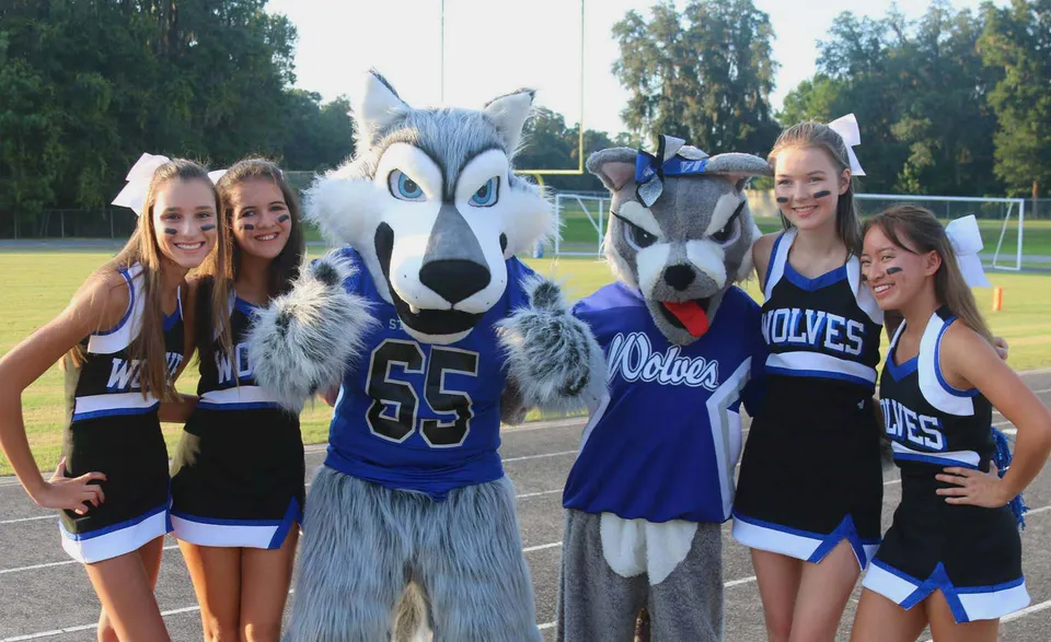 Un gruppo di studentesse della Saint Francis Catholic Academy posa sul campo sportivo con la mascotte in divisa sportiva.