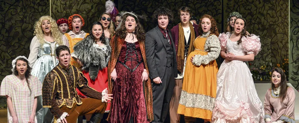 Studenti della St. Mary's Ryken High School mettono in scena uno spettacolo teatrale in costumi colorati su un palco con uno sfondo scuro.
