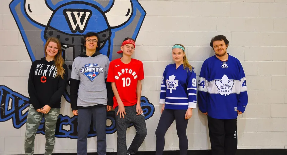 Un gruppo di studenti della WillowWood School in posa davanti a un grande murale sportivo.