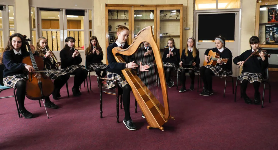Un gruppo di studenti di musica, tra cui un'arpista, è in piedi in un'aula del campus del Mercy College.