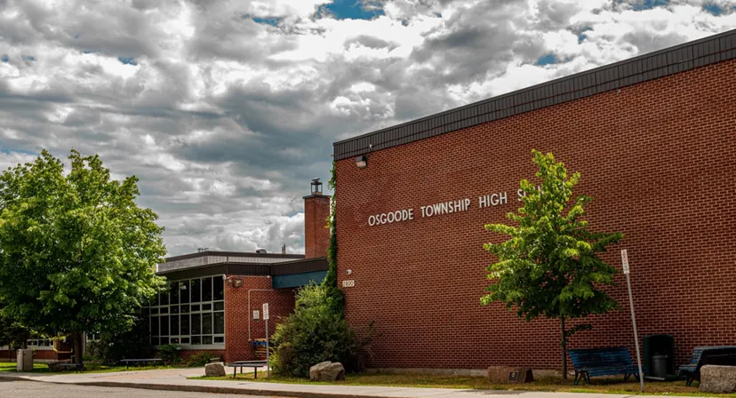 L'edificio in mattoni della Osgoode Township High School è circondato da alberi sotto un cielo nuvoloso.