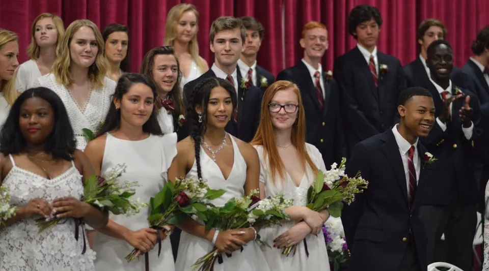 Un gruppo di studenti della St. Anne's-Belfield School è davanti a un sipario rosso e tiene dei fiori durante la cerimonia di diploma.