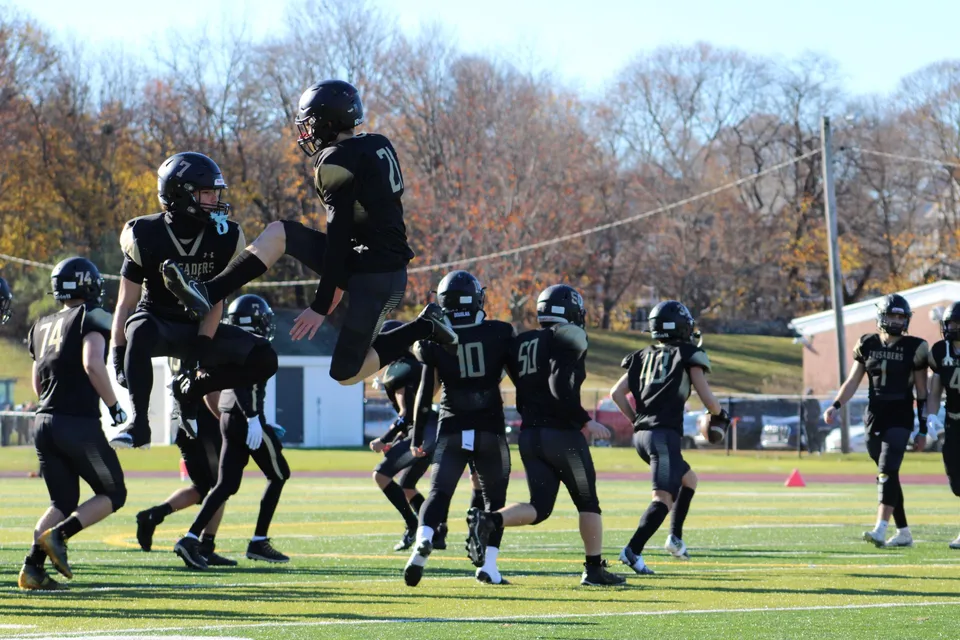 Giocatori di football americano della Bishop Fenwick High School saltano in aria durante una partita sul campo.
