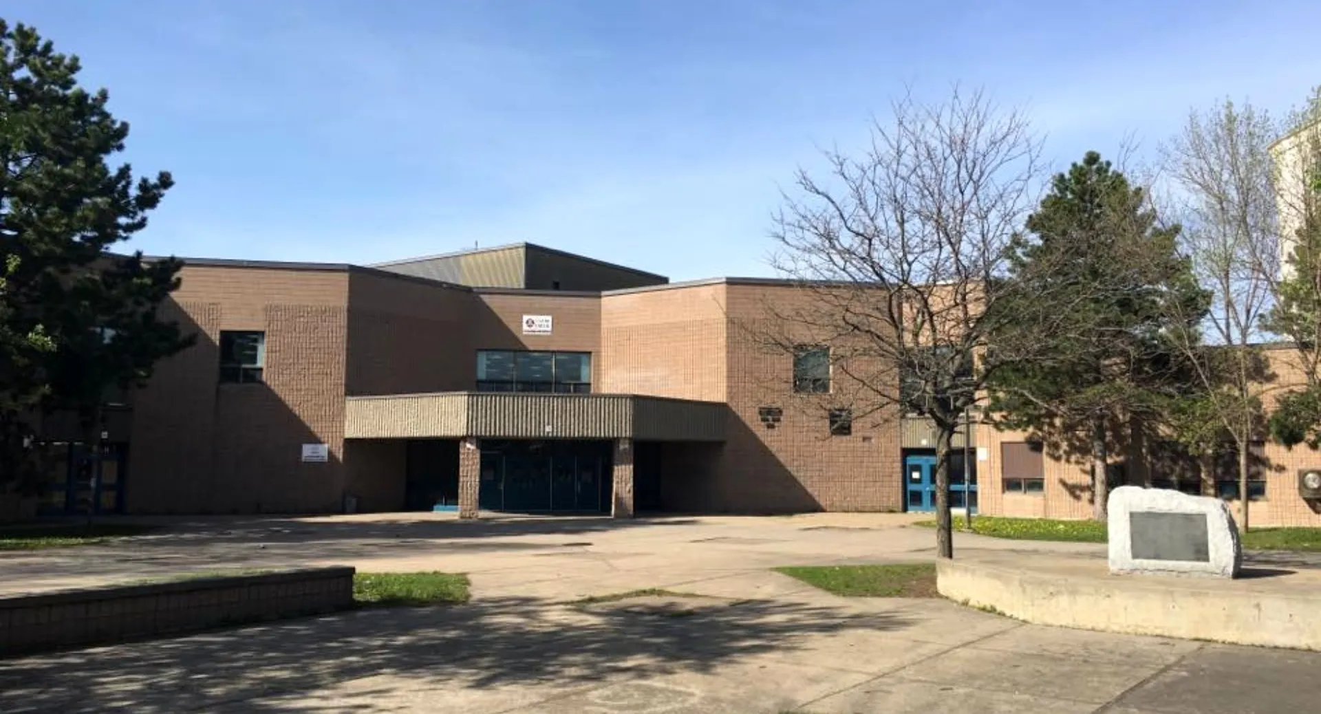 L'edificio moderno in mattoni con ingresso a vetri della Laurier MacDonald High School è circondato da alberi e da un'area pavimentata.