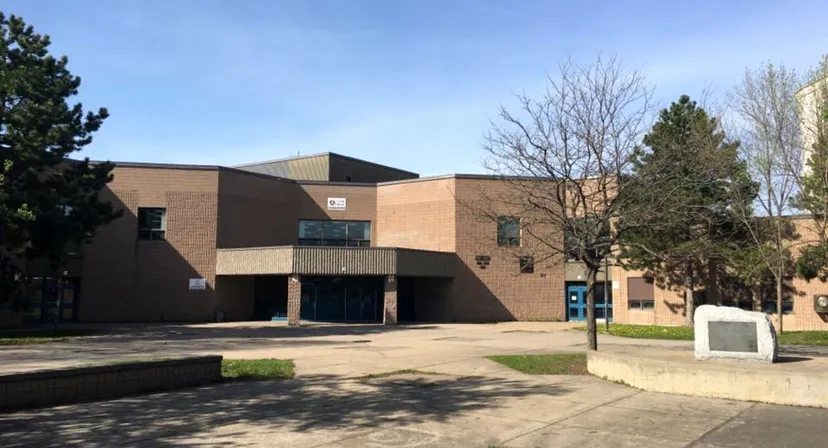 L'edificio moderno in mattoni con ingresso a vetri della Laurier MacDonald High School è circondato da alberi e da un'area pavimentata.