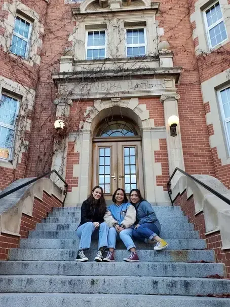 Tre studentesse sedute sulla scalinata di una scuola in mattoni rossi