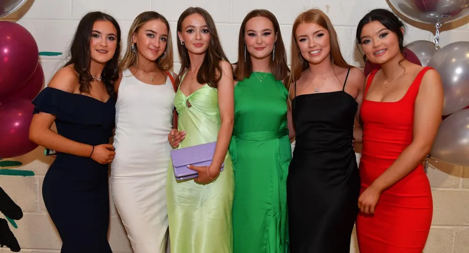 Sei studentesse della Carrick on Shannon Community School in posa insieme a un evento scolastico con decorazioni sullo sfondo.