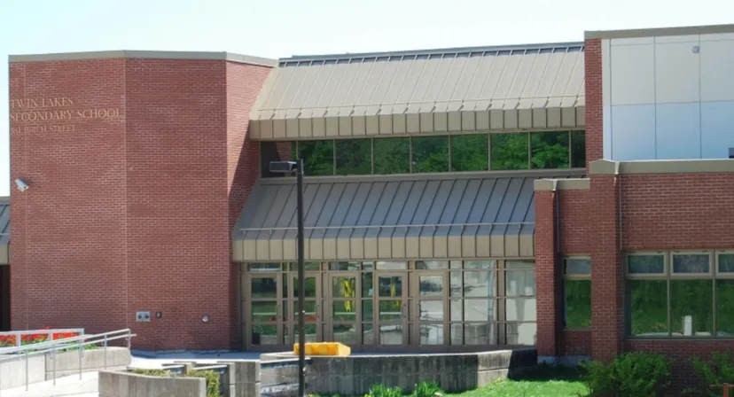 L'edificio in mattoni della Twin Lakes Secondary School con vetrate e una pensilina in metallo, circondato da aree verdi e un piazzale pavimentato.