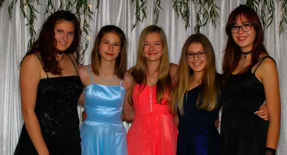 Cinque giovani donne in abito formale posano insieme davanti a una tenda nel campus della Springbank School.
