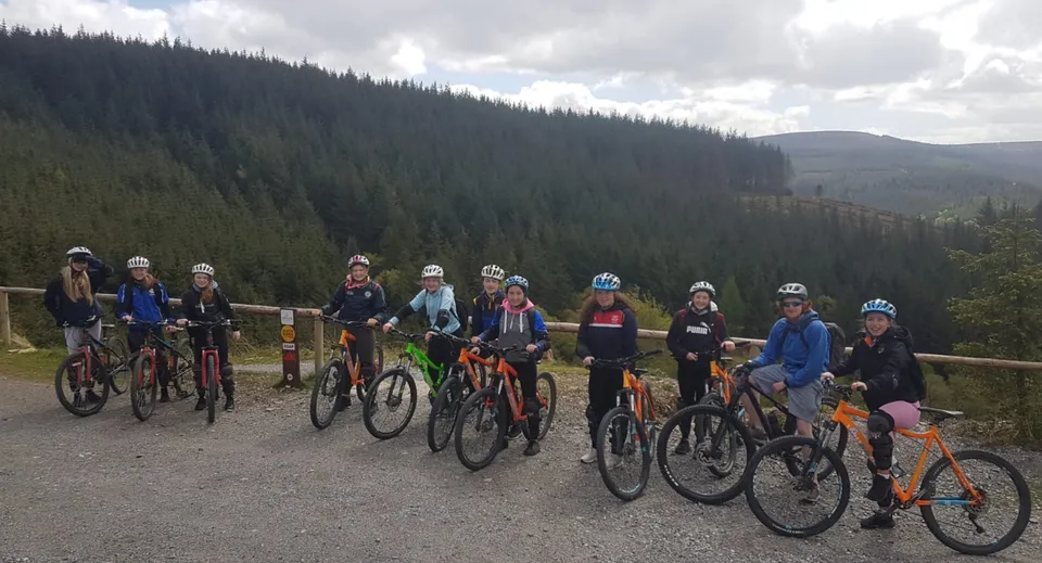 Un gruppo di studenti in bicicletta si trova su un sentiero boschivo nel campus del Banagher College sotto un cielo nuvoloso.
