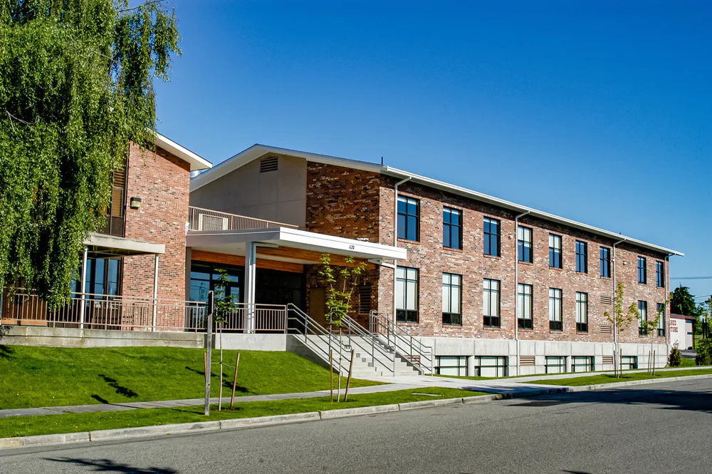 El moderno edificio de ladrillo de Covenant High School con grandes ventanas está frente a un césped bajo un cielo azul.