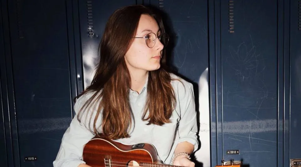 Una studentessa della Polyvalente Roland-Pépin tiene una chitarra acustica davanti a una parete blu scuro.