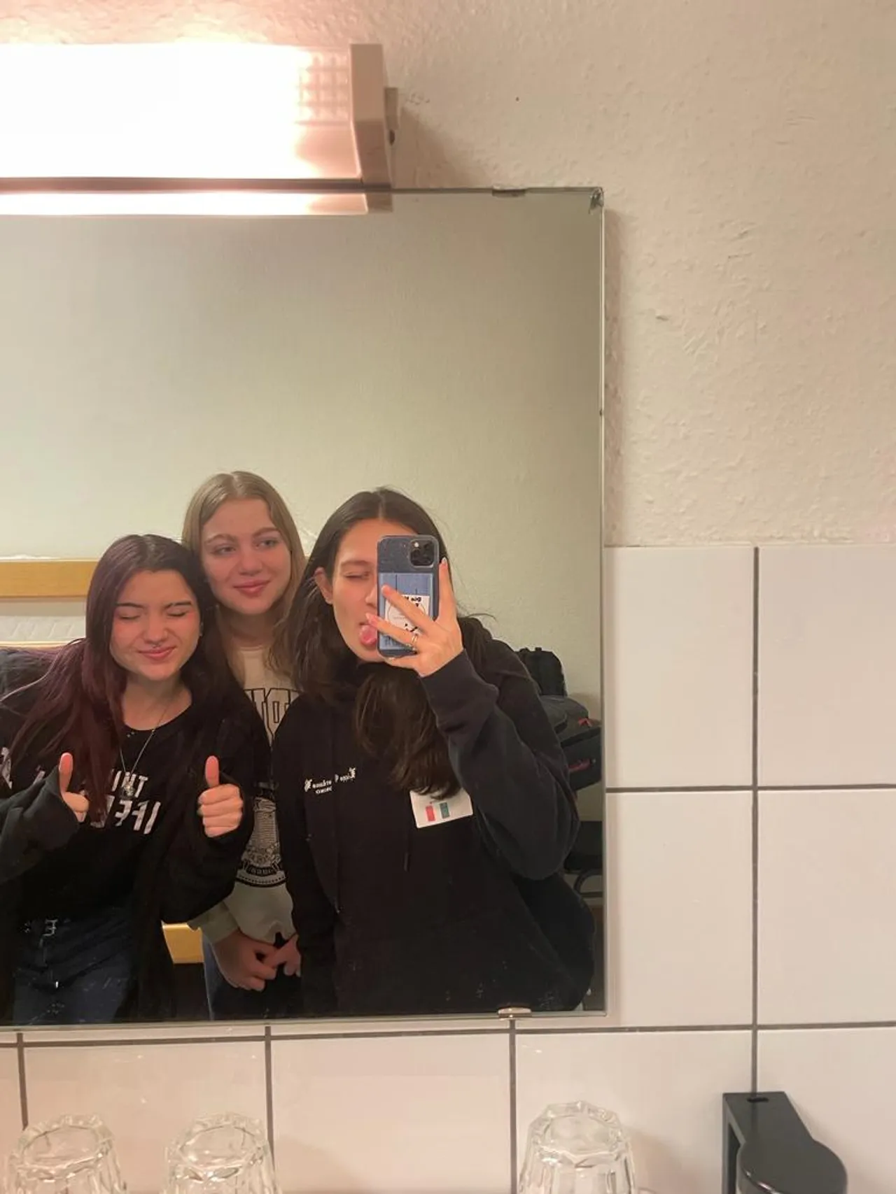 Tre ragazze si scattano un selfie allo specchio facendo il pollice in su
