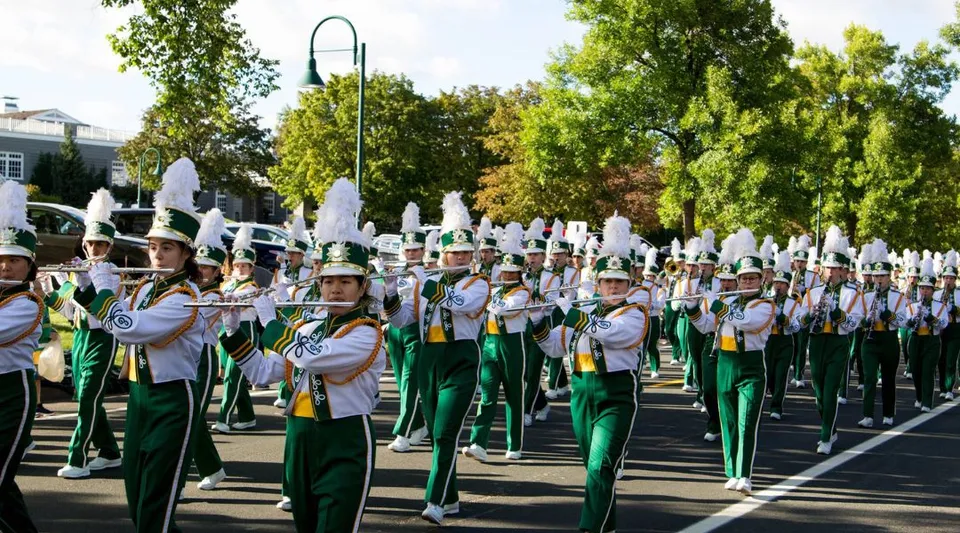 La Marching Band delle Edina Public Schools si esibisce in uniforme verde e bianca lungo una strada alberata.
