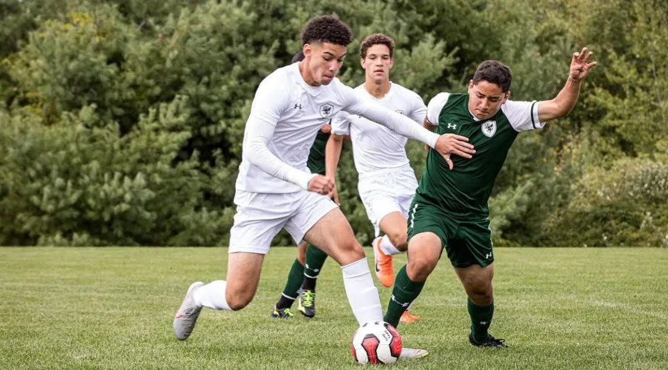 Due studenti giocano a calcio sul campo sportivo della High Mowing School davanti a una zona boscosa.