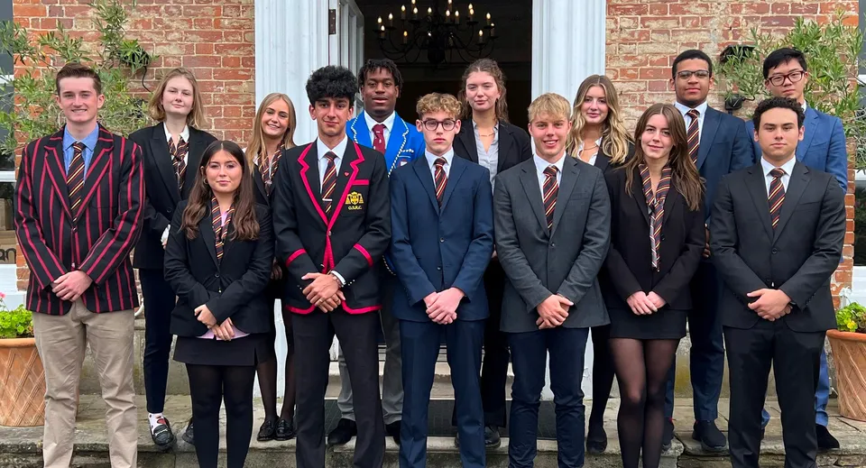 Un gruppo di studenti della The Oratory School in abito formale si trova davanti a un edificio in mattoni con un lampadario all'ingresso.