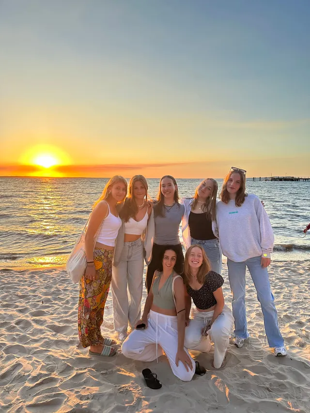 Grupo de chicas posando juntas en la playa durante la puesta de sol