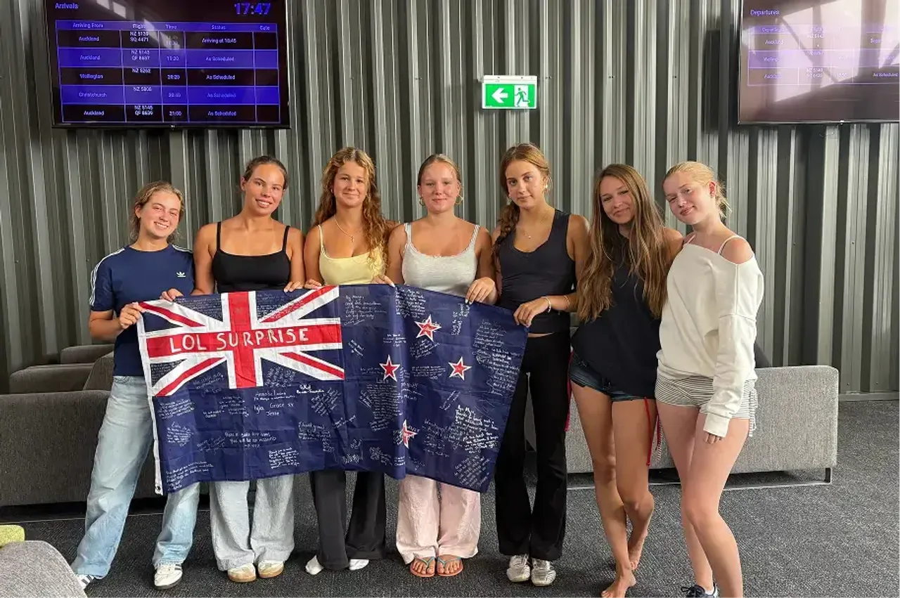 Gruppo di studentesse con una bandiera della Nuova Zelanda firmata all'aeroporto