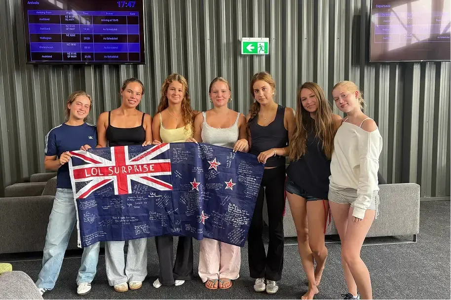 Gruppo di studentesse con una bandiera della Nuova Zelanda firmata all'aeroporto