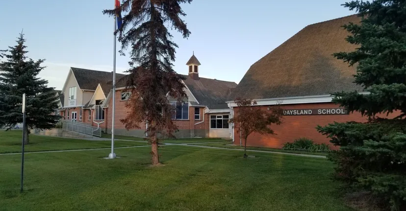L'edificio in mattoni della Daysland School con campanile si trova su un'area erbosa circondata da alberi sotto un cielo azzurro.