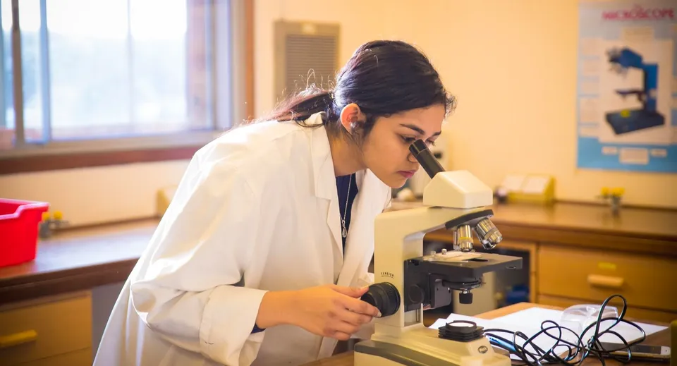 Una persona con il camice bianco da laboratorio utilizza un microscopio nel laboratorio del Cambridge Tutors College.