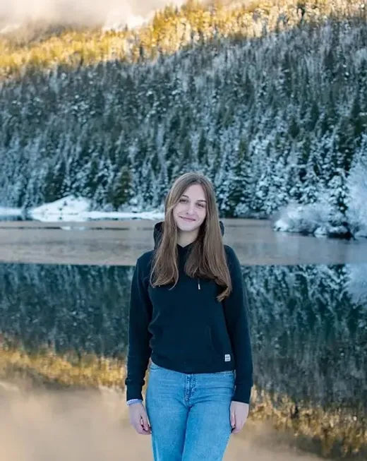 Ragazza sorridente davanti a un lago di montagna circondato da boschi innevati