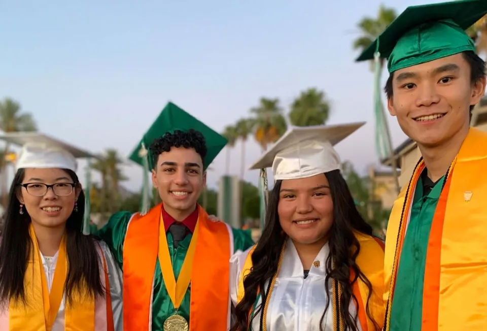 Un gruppo di studenti della Phoenix Christian Preparatory School è in posa con le toghe da diploma davanti a un paesaggio suggestivo con palme.