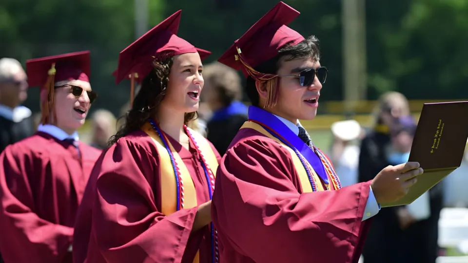 Un gruppo di diplomati della St. Joseph High School è all'aperto in toga e tocco rossi e tiene in mano i propri diplomi.