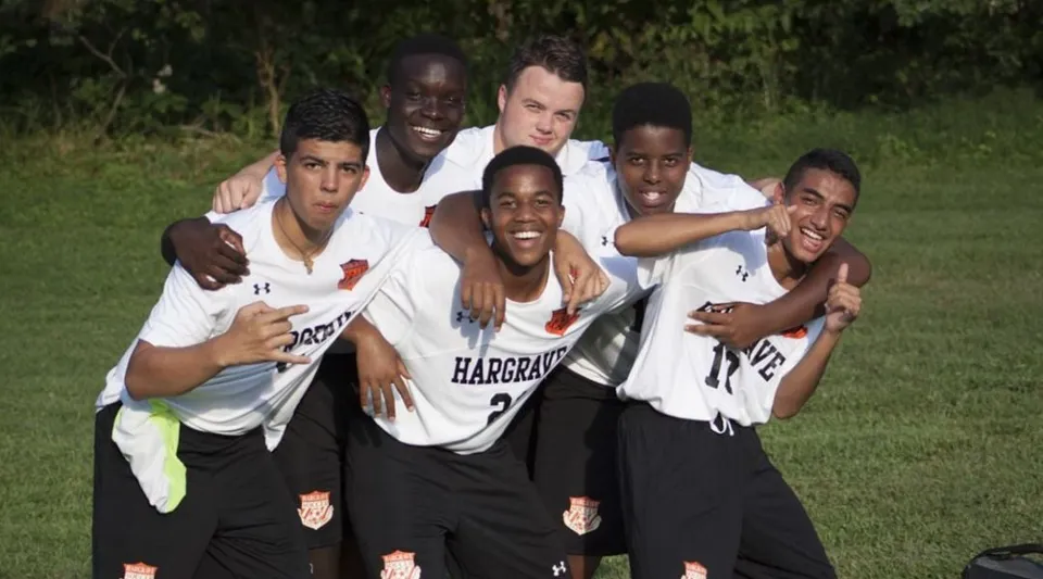 Un gruppo di studenti in divisa sportiva si abbraccia e sorride su un campo erboso della Hargrave Military Academy.
