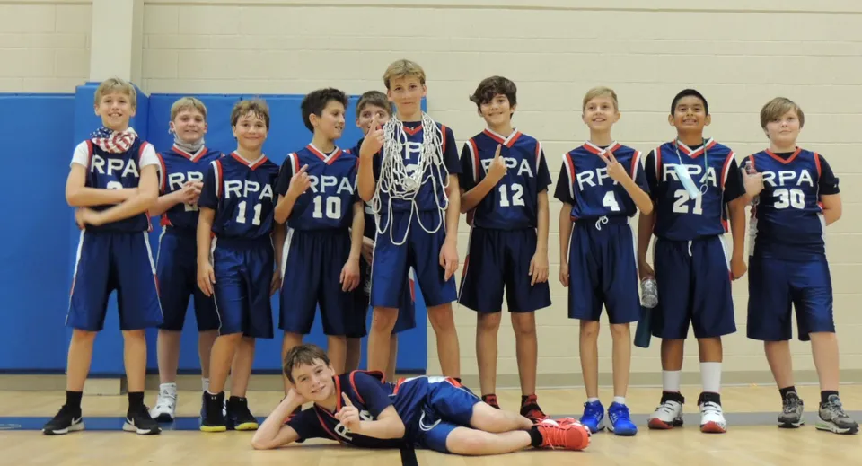Un gruppo di studenti e studentesse della Royal Palm Academy posa in palestra con le proprie divise blu da basket.