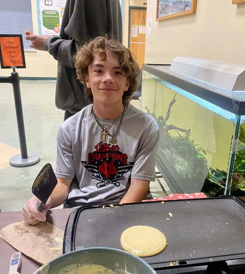 Uno studente della Cedar Community Secondary School tiene una spatola accanto a una piastra elettrica mentre cucina dei pancake.