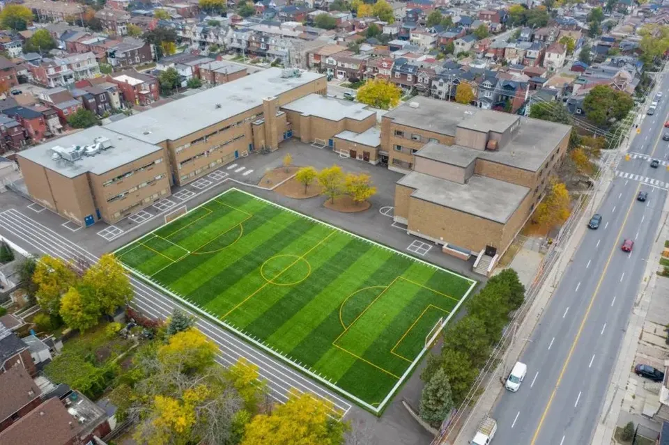 Il grande campo da calcio verde nel campus del Hudson College, con edifici e una strada trafficata sullo sfondo.