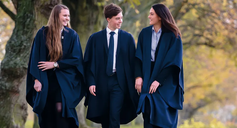 Tre studenti della Felsted School si trovano nel bosco e indossano toghe accademiche scure.