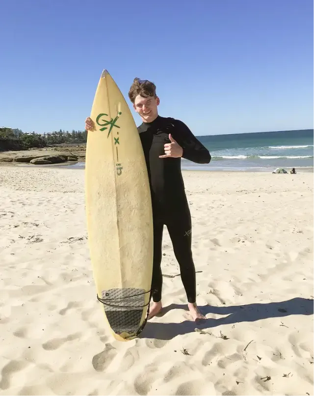 Ragazzo in muta con la tavola da surf su una spiaggia australiana