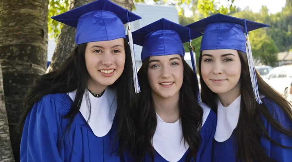 Tre studentesse della Caledonia Secondary School in abito da cerimonia blu in posa insieme nel bosco.